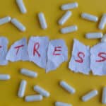 The word "stress" made from torn pieces of paper surrounded by pills indicating the stress of addiction and the stress of recovery.