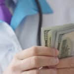 Doctor with stethoscope in a lab coat counting out hundred-dollar bills is representative of corporations pushing addiction.
