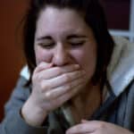 Photo of a woman throwing up into her hand, a symptom of Cannabinoid Hyperemesis Syndrome.