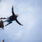 a woman takes a giant leap with the assistance of a friend and bungee cord
