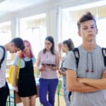 Photo of mean-looking teenage boy in class with a background group of teenage classmates.