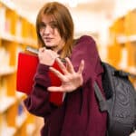 Female high school student wearing backpack and carrying notebooks holds her hand out in a sign of resistance to substance abuse.