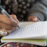 Close up photograph of a woman's hands writing with a pen in a journal.