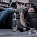 Photo of a drunken young woman asleep on a couch surrounded by alcohol bottles.