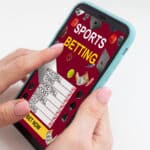 Photograph of hands holding a smartphone that is open to a sports betting application.