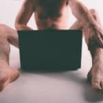Photo of young naked man watching pornography and masturbating.
