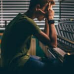 Photo of college student with his head in his hands and his elbows on an upright piano illustrating the stress cause by an addiction to playing music.