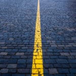 Photograph of brick paving, painted blue, with a yellow line down the center, indicated the line between substance use and substance abuse.