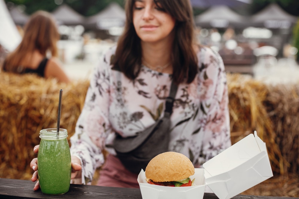 Photo of a young woman resisting the visual cue of a hamburger and picking up an organic smoothie instead.