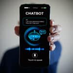 Photo of a hand holding smartphone with a digital AI chatbot on the screen.