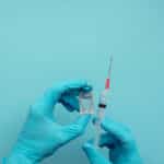 Photo of hands wearing blue surgical gloves holding a syringe and vaccine dose.