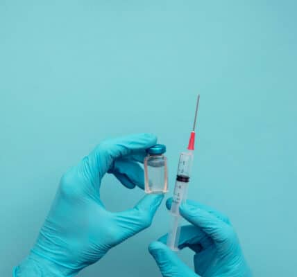 Photo of hands wearing blue surgical gloves holding a syringe and vaccine dose.