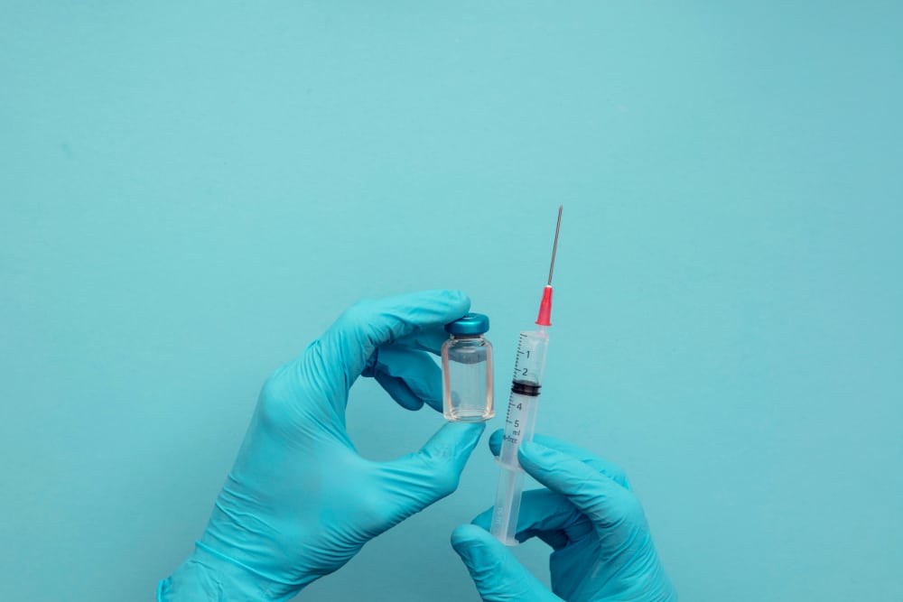 Photo of hands wearing blue surgical gloves holding a syringe and vaccine dose.