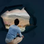 Surreal image includes photo of a man crouching down and looking out through a 360-degree window at a beautiful landscape representing addiction recovery.