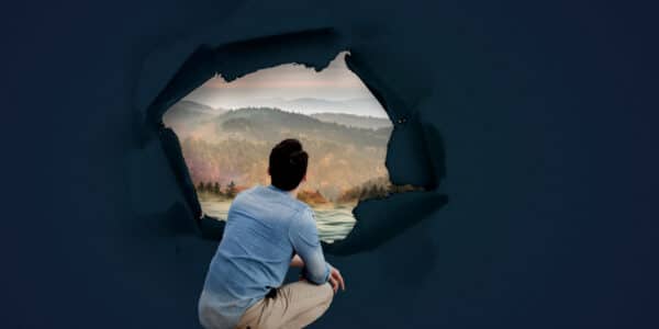 Surreal image includes photo of a man crouching down and looking out through a 360-degree window at a beautiful landscape representing addiction recovery.