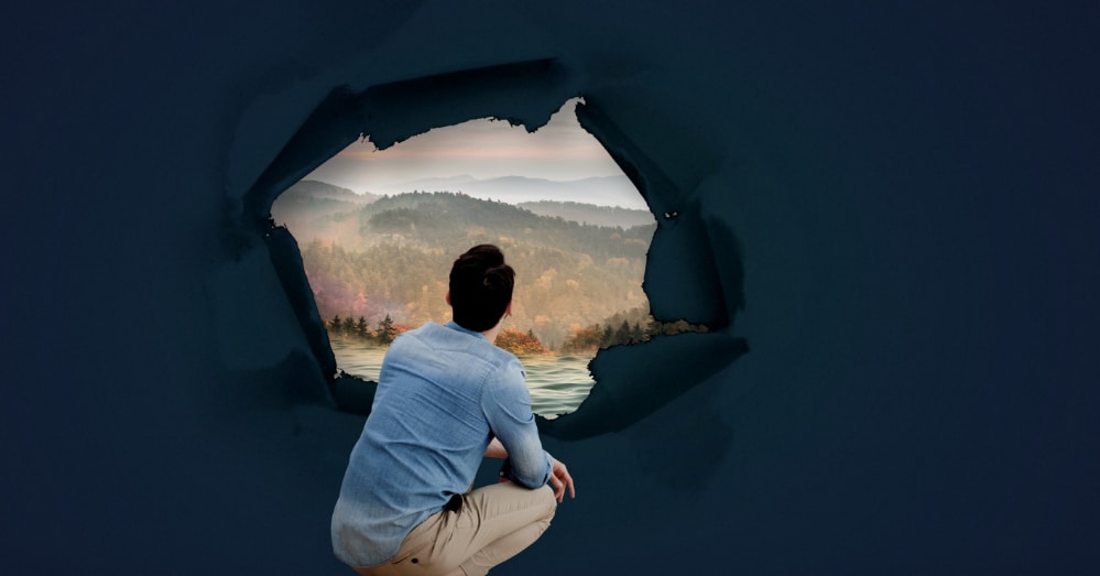 Surreal image includes photo of a man crouching down and looking out through a 360-degree window at a beautiful landscape representing addiction recovery.