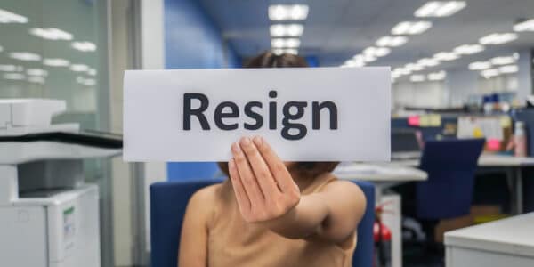 Photo of woman in an office holding up a sign with the word, "Resign."