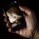 Photo of a young man's hand holding a smartphone displaying an erotic embrace.