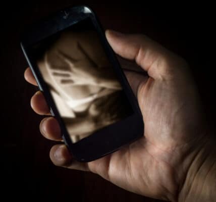 Photo of a young man's hand holding a smartphone displaying an erotic embrace.