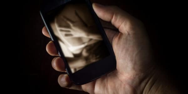 Photo of a young man's hand holding a smartphone displaying an erotic embrace.