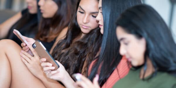 Group of five teen girls using their smart phones.