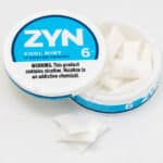 Photo shows an open can of ZYN Nicotine Pouches in Cool Mint flavor with three pouches stacked outside the tin.