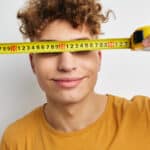 Photo of a boy holding a tape measure in front of his eyes symbolizing the correlation between brain size and substance abuse.