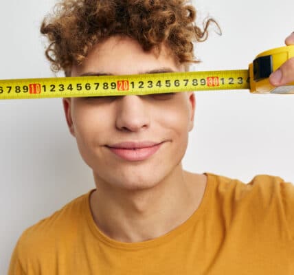 Photo of a boy holding a tape measure in front of his eyes symbolizing the correlation between brain size and substance abuse.