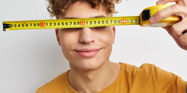 Photo of a boy holding a tape measure in front of his eyes symbolizing the correlation between brain size and substance abuse.