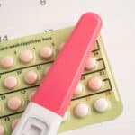Photo of a pregnancy test on top of a blister pack if birth control pills on top of a calendar.