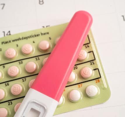 Photo of a pregnancy test on top of a blister pack if birth control pills on top of a calendar.