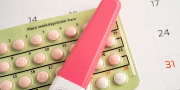 Photo of a pregnancy test on top of a blister pack if birth control pills on top of a calendar.