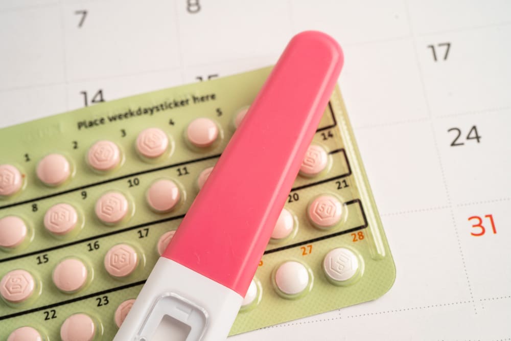 Photo of a pregnancy test on top of a blister pack if birth control pills on top of a calendar.
