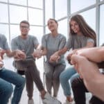 Photo of teenagers sitting in a support circle holding hands at a recovery high school.