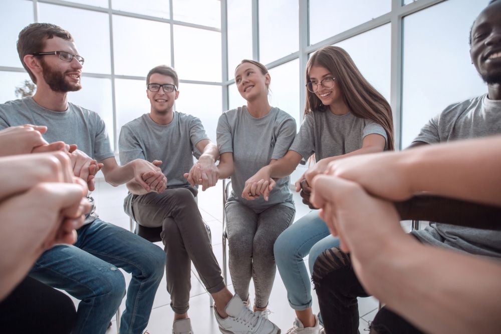 Photo of teenagers sitting in a support circle holding hands at a recovery high school.