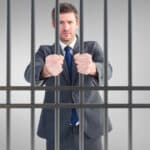 Photo of man in business suit behind bars, the result of civil commitment for people suffering substance use disorders.