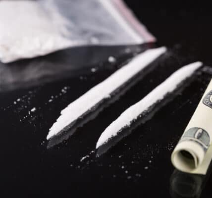 Photograph of cocaine on a table in a bag and in two lines next to a rolled-up one hundred dollar bill.