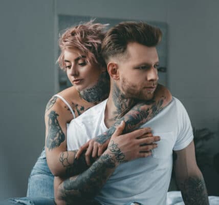 Photograph of a young man being embraced by a young woman, both heavily tattooed.