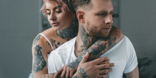 Photograph of a young man being embraced by a young woman, both heavily tattooed.