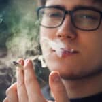 Photograph of a young man smoking a marijuana cigarette.
