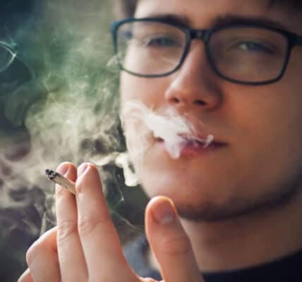 Photograph of a young man smoking a marijuana cigarette.