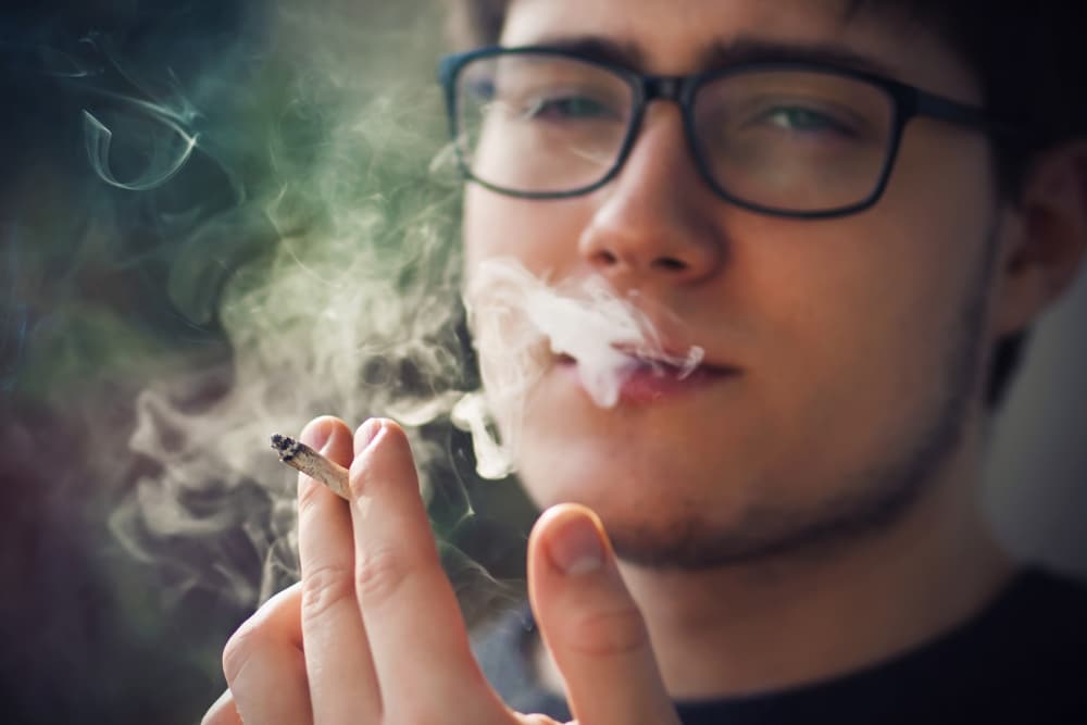 Photograph of a young man smoking a marijuana cigarette.