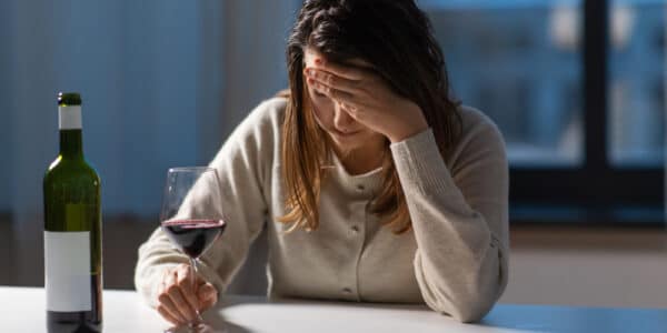 Photograph of a depressed mother with her head in her hand drinking wine.