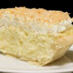 Photo of a slice of coconut cream pie on a white plate, meant to induce cravings.