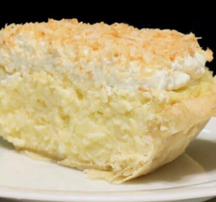 Photo of a slice of coconut cream pie on a white plate, meant to induce cravings.