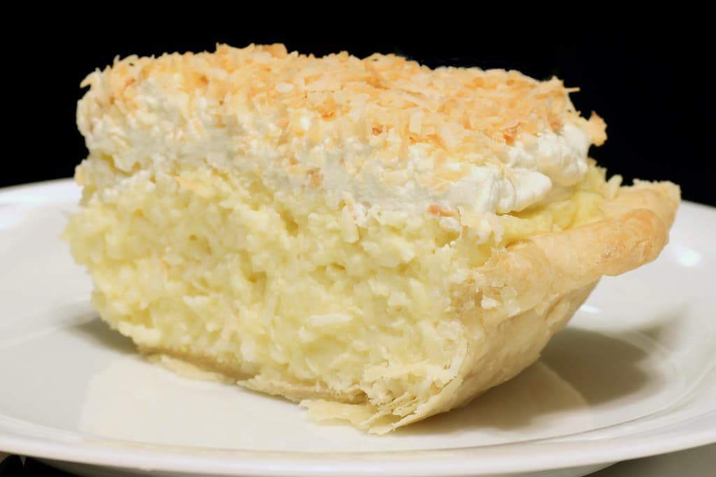 Photo of a slice of coconut cream pie on a white plate, meant to induce cravings.