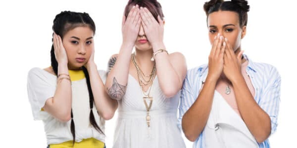 Photograph of three young, ethnically diverse women covering their ears, eyes, and mouth similar to the "hear no evil, see no evil, speak no evil" meme.