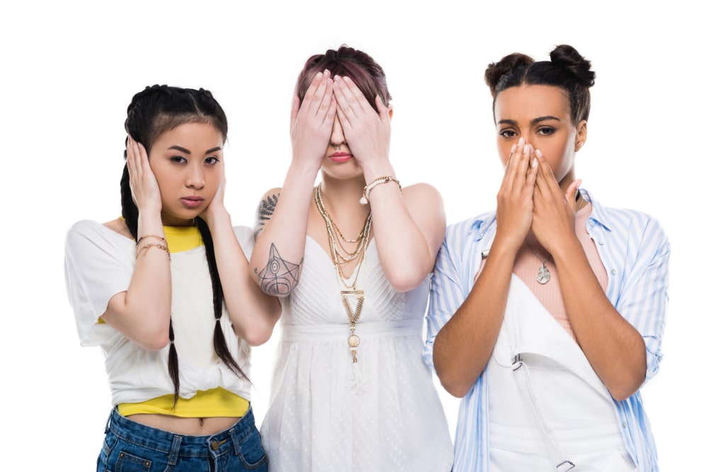 Photograph of three young, ethnically diverse women covering their ears, eyes, and mouth similar to the "hear no evil, see no evil, speak no evil" meme.
