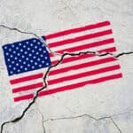 Photograph of an American flag painted onto a sidewalk that has cracked, fracturing the flag.