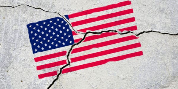 Photograph of an American flag painted onto a sidewalk that has cracked, fracturing the flag.